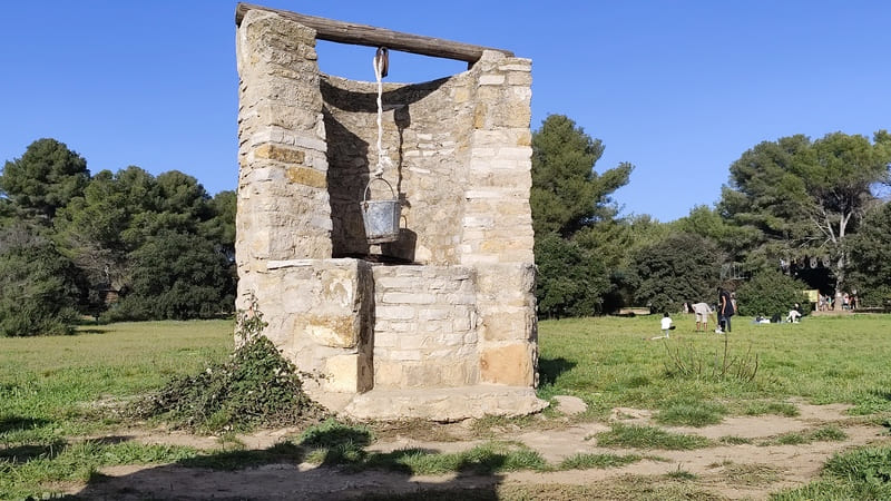 El patrimonio agrícola, dedicado al agua dulce, se exhibe en el Gran Parque de Figuerolles, Martigues. Un cubo cuelga de un pozo en medio de una pradera. - © Otmartigues / MyriamF
