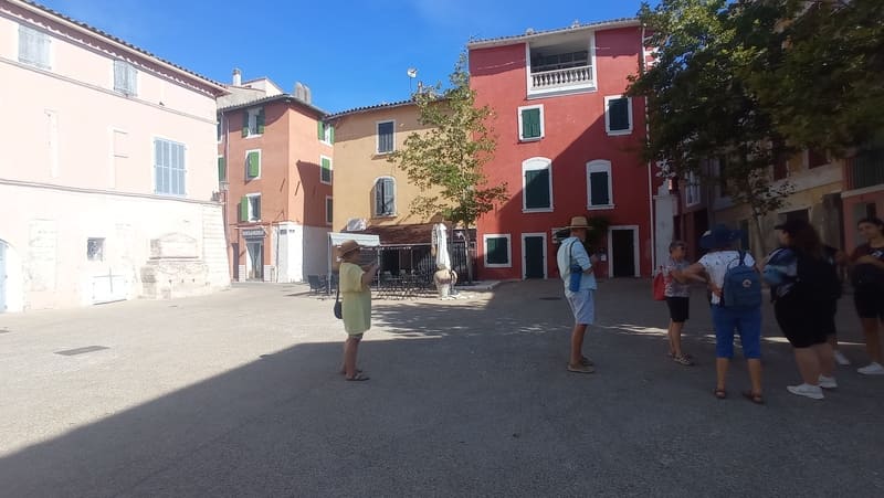 Participants à une visite du centre-ville de Martigues sur la place Mirabeau, ses façades colorées et sa fontaine mythique. Une partie de la place est ombragée par les platanes - © Otmartigues / MyriamF