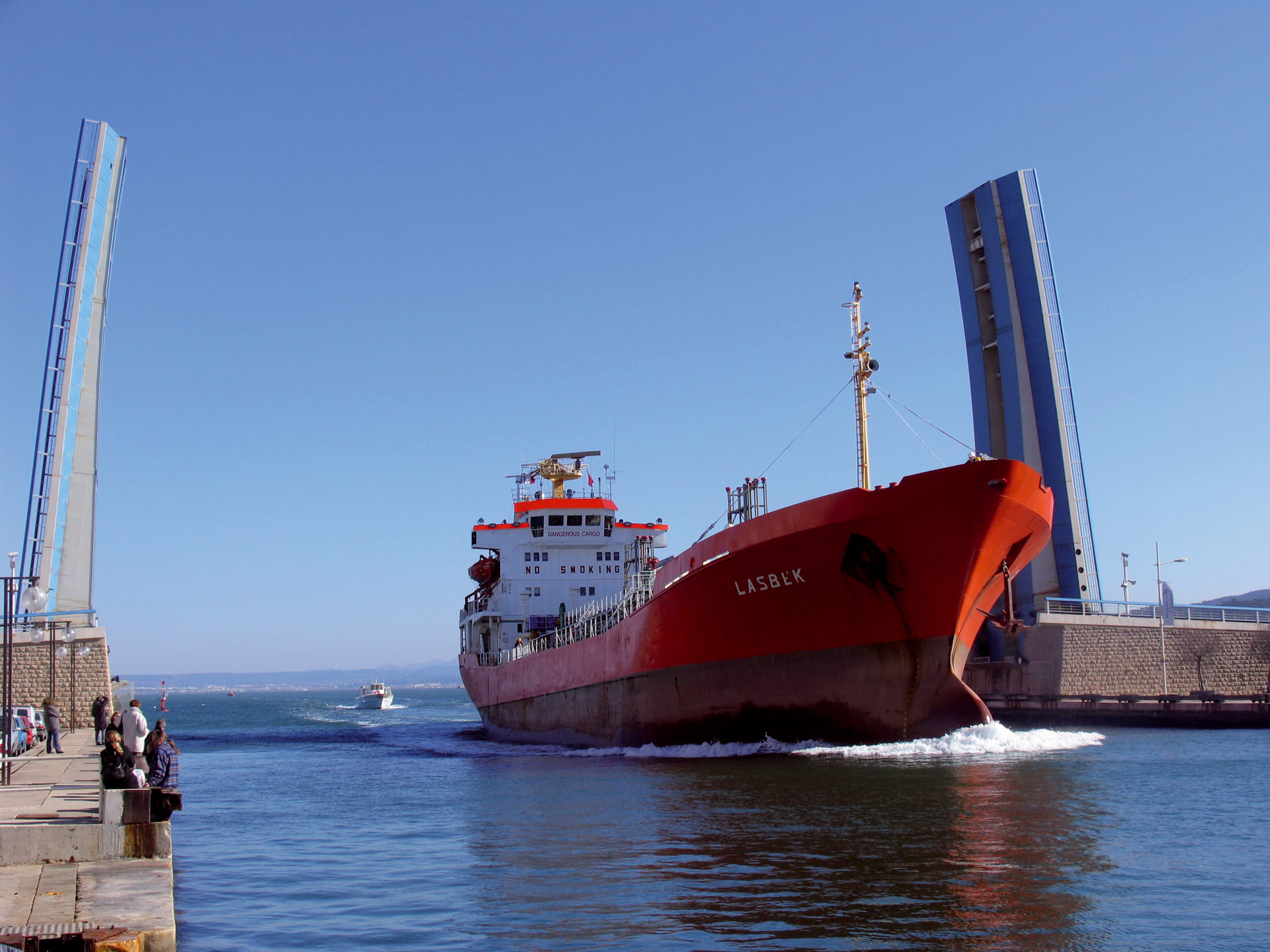 Ein Frachtschiff mit rotem Rumpf überquert den Martigues-Kanal, während Passanten zuschauen. Die Hubbrücke zwischen dem Étang de Berre und dem Mittelmeer ist geöffnet. - © Otmartigues / SergeT