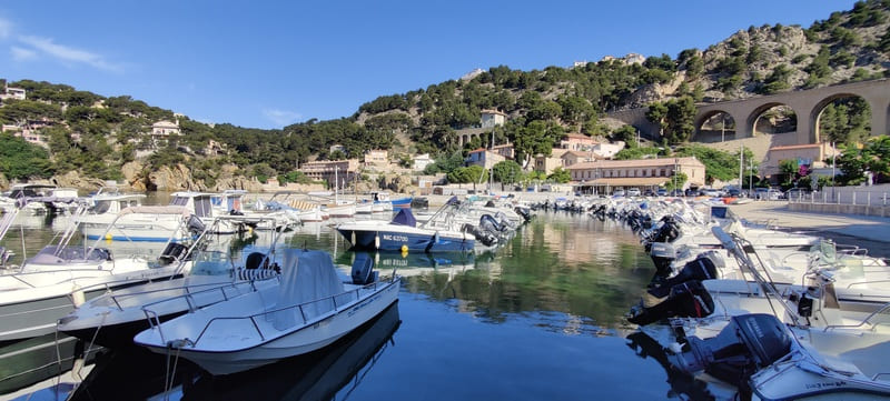Reflections of boats moored at the Port of Niolon with the wild green hills, the railway bridge, and Niolon Cove in the background - © Otmartigues / SergeT
