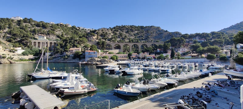 Port of Niolon pontoon with moored boats, the railway bridge crossed by the Côte Bleue blue train, and the lush green hills surrounded by nature - © Otmartigues / SergeT