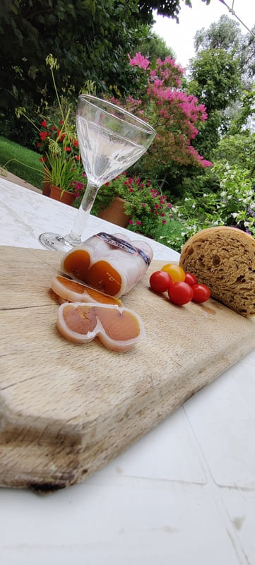 Boutargo sliced into strips on a wooden board, a stemmed glass placed next to it, and a loaf of bread as an aperitif in Martigues. - © Otmartigues / SergeT