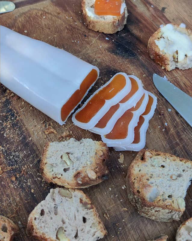 Boutargo sliced into thin strips next to thick slices of bread. The blade of a knife is visible on the wooden board. The bottarga is still wrapped in wax. - © Otmartigues / SergeT